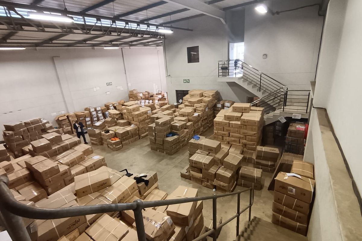 Large commercial warehouse space featuring high ceilings with exposed steel trusses, concrete flooring, and an internal metal staircase leading to an upper level.