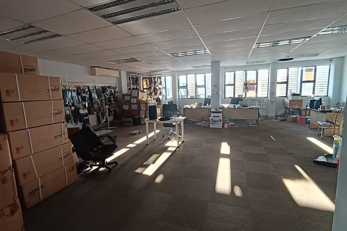 Open-plan commercial office space featuring suspended ceilings, recessed lighting, wall-mounted air conditioning, and large windows providing natural light.