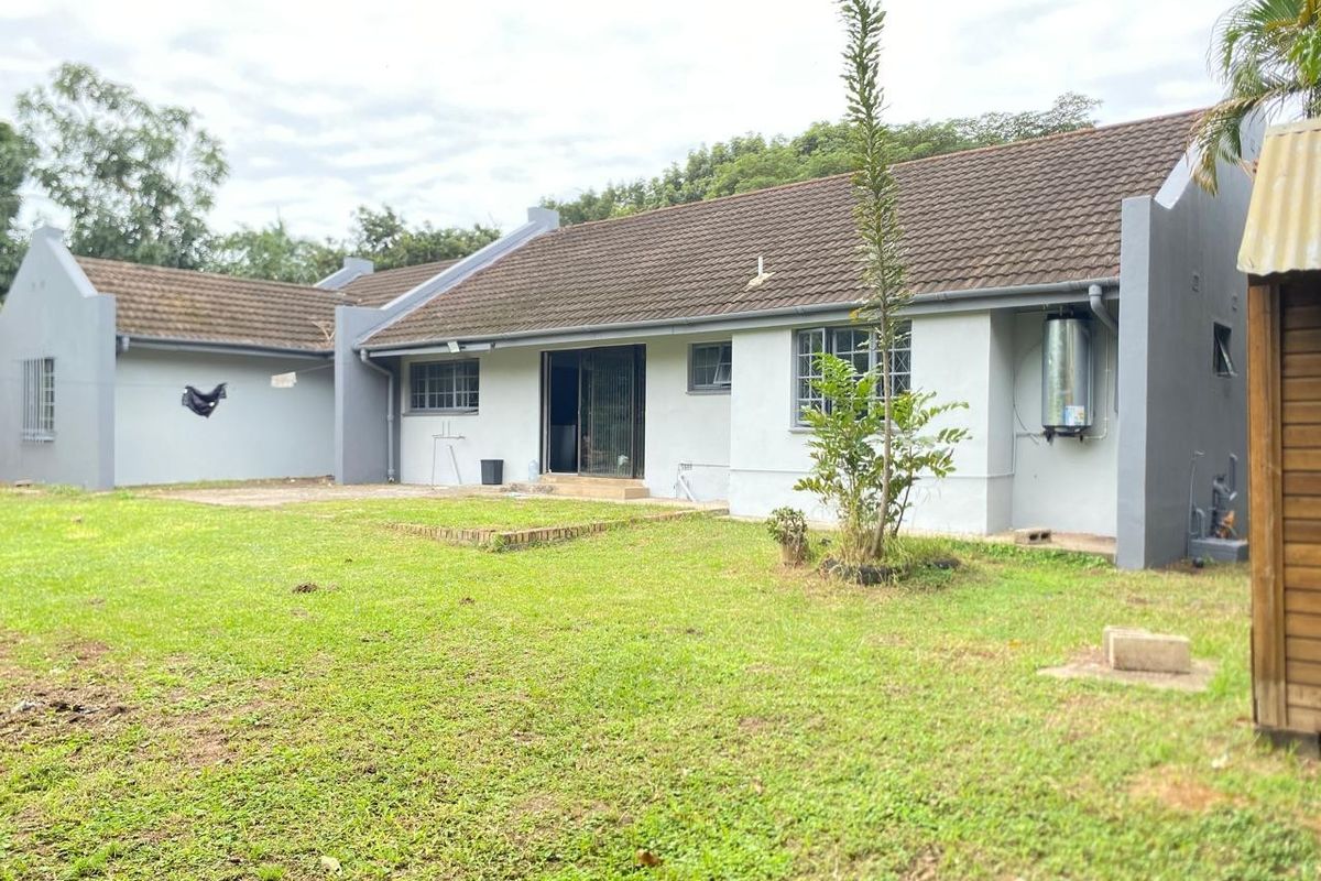 Rear view of a single-story house featuring a tiled roof, external geyser, and a spacious backyard with a concrete patio area.