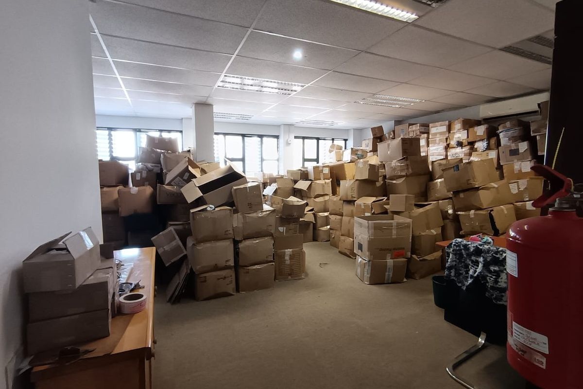 Commercial office space featuring a suspended ceiling, fluorescent lighting, and carpeted flooring, currently utilized for storage.