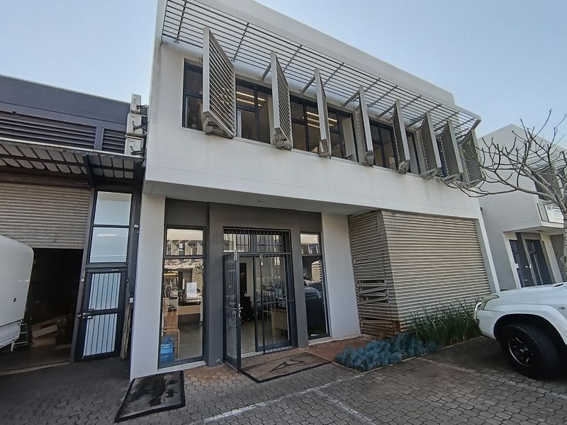 Front facade of a commercial property featuring modern louvre shutters, glass entrance, and paved parking area.