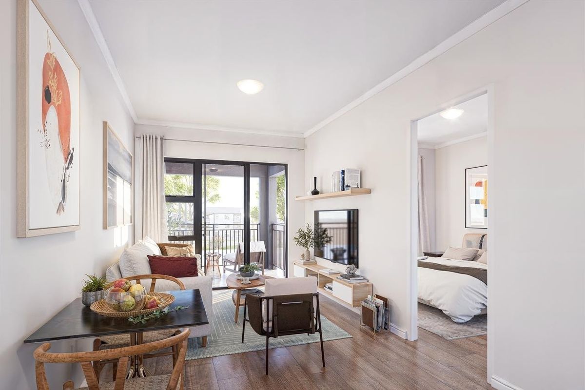 Bright open-plan living area featuring modern laminate flooring, a floating media shelf, and direct access to a private balcony through sliding glass doors.