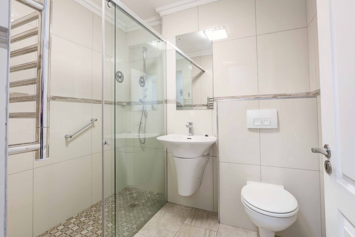 Modern, well-maintained bathroom featuring a glass shower enclosure, wall-mounted basin, wall-hung toilet, and a heated towel rail with neutral tiling throughout.