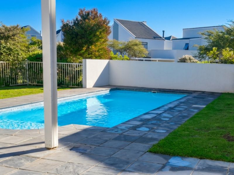 A private swimming pool area featuring stone paving, perimeter fencing, and a landscaped garden setting within a residential complex.