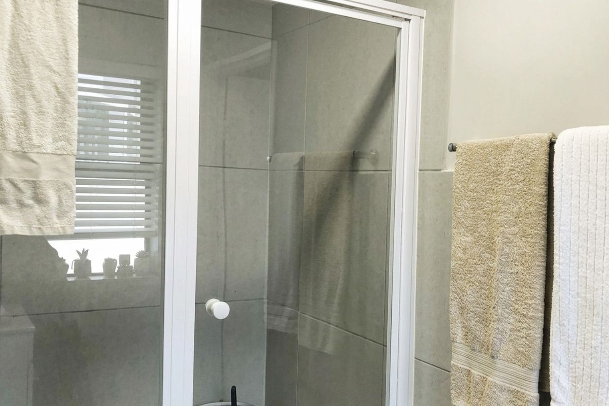 A functional bathroom featuring a glass shower enclosure with white framing, neutral wall tiling, and a wall-mounted towel rail.