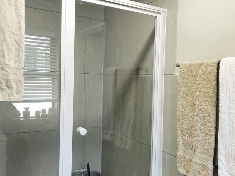 A functional bathroom featuring a glass shower enclosure with white framing, neutral wall tiling, and a wall-mounted towel rail.