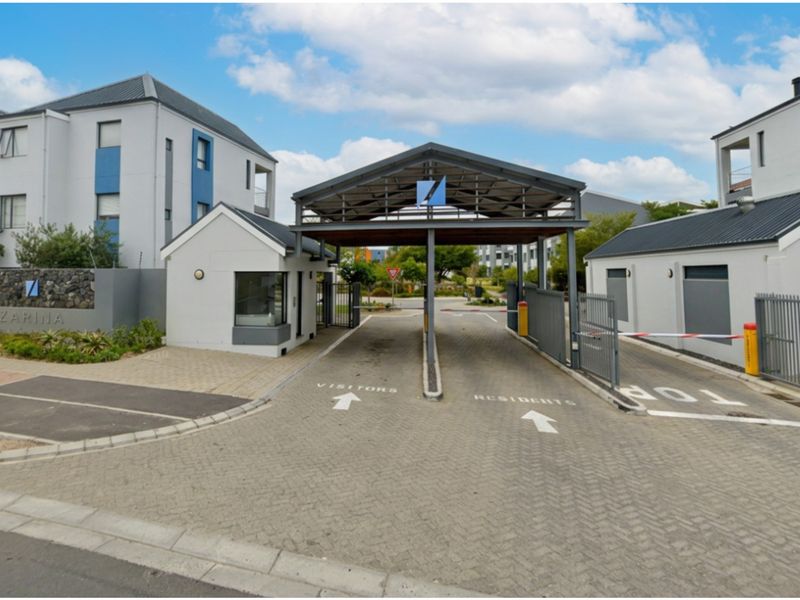 The secure entrance to the apartment complex features a gated access point with a dedicated security guardhouse and paved driveway for residents and visitors.
