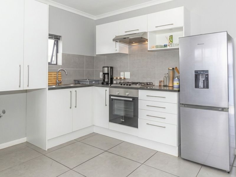 Modern kitchen featuring white cabinetry, stainless steel appliances including a gas hob and oven, tiled backsplash, and neutral floor tiles.