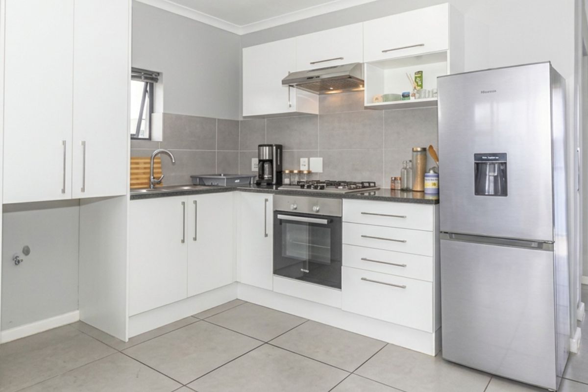 Modern kitchen featuring white cabinetry, stainless steel appliances including a gas hob and oven, tiled backsplash, and neutral floor tiles.