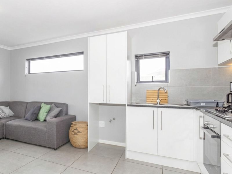 Modern open-plan living area featuring a compact kitchen with built-in cabinetry, stainless steel appliances, and neutral tiled flooring throughout.