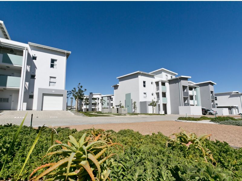 A view of a modern apartment complex featuring paved driveways, garage access, and well-maintained exterior facades under a clear blue sky.