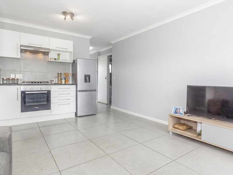 Modern open-plan living area featuring a sleek kitchen with built-in appliances and neutral tiled flooring throughout.
