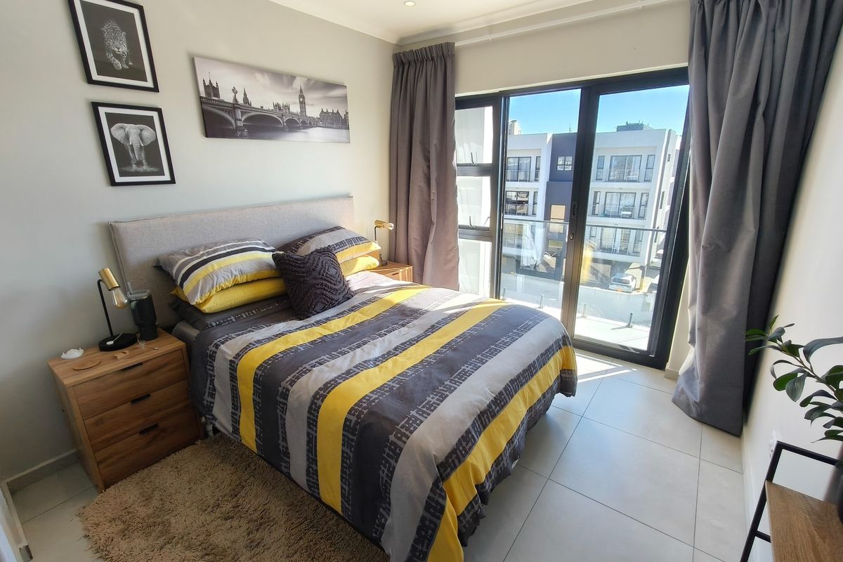 A well-lit bedroom featuring tiled flooring, recessed ceiling lights, and a large sliding glass door providing access to a balcony.