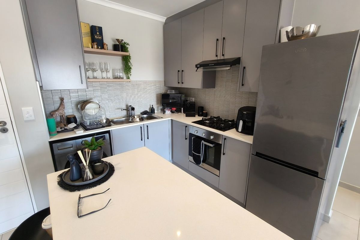Modern kitchen featuring sleek grey cabinetry, stone countertops, a central island, and integrated appliances including a built-in oven and gas hob.
