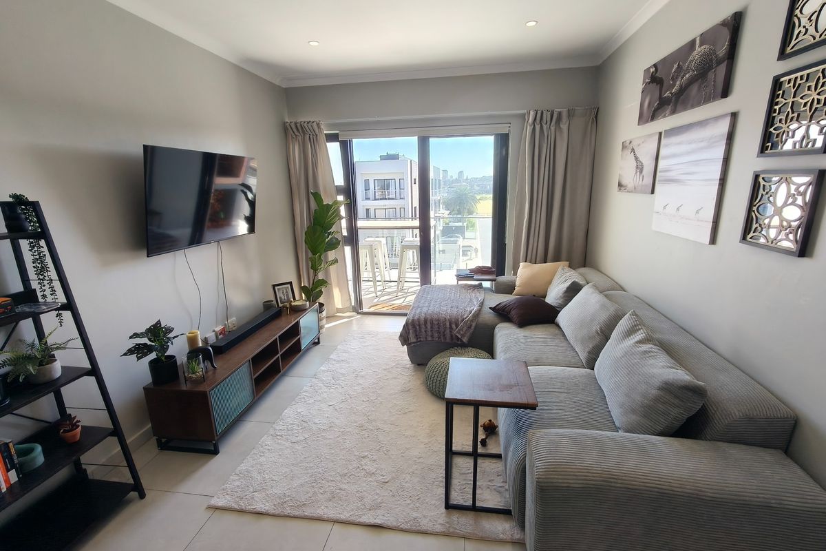 A well-maintained living room featuring tiled flooring, recessed downlighting, and a sliding glass door providing access to a private balcony.