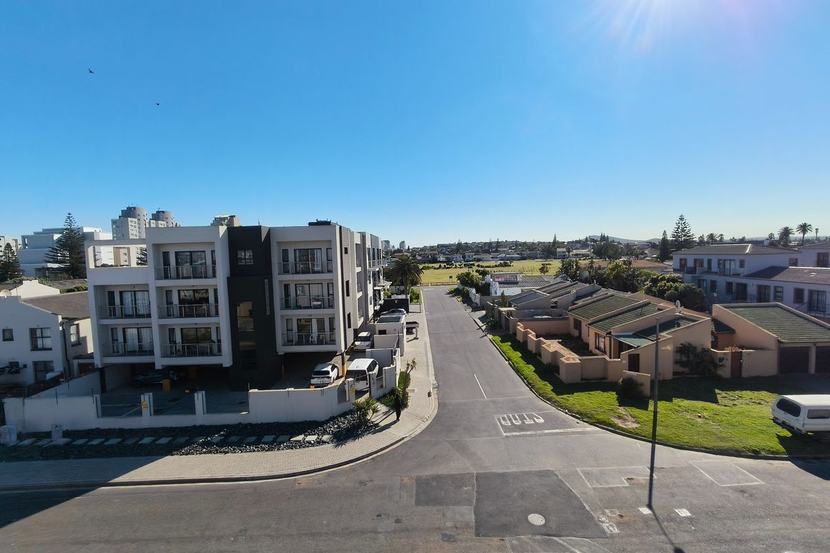 An elevated aerial view of a residential street featuring a modern apartment complex and surrounding suburban neighborhood infrastructure.