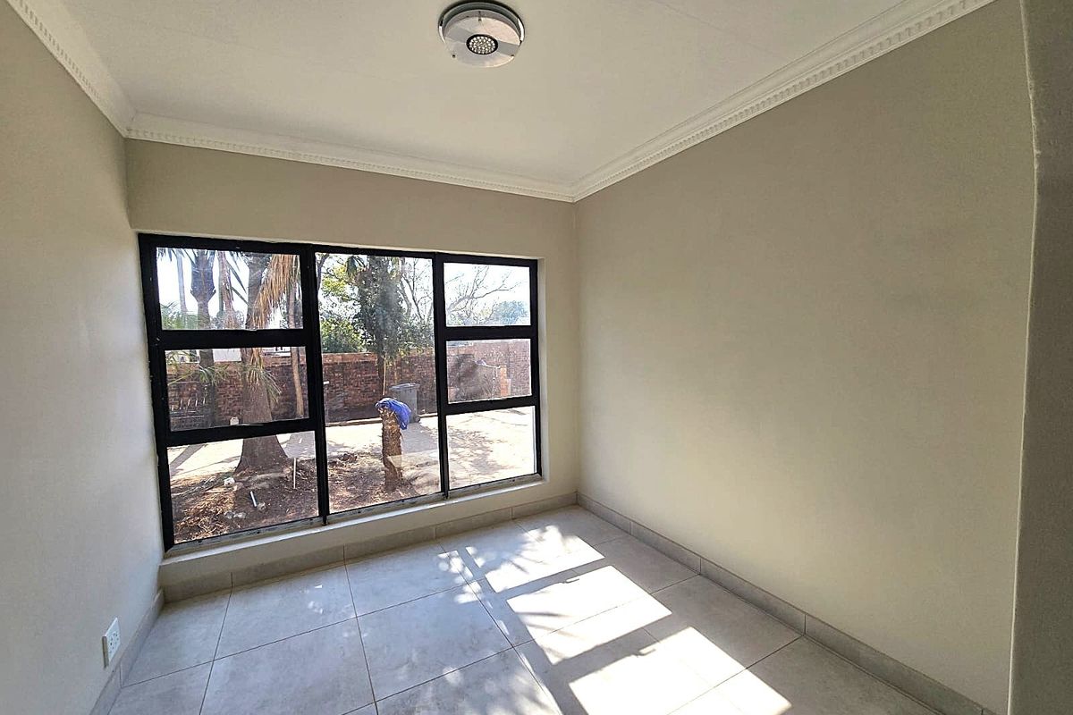 A bright, empty bedroom featuring neutral tiled flooring, black aluminium window frames, and decorative ceiling cornicing.