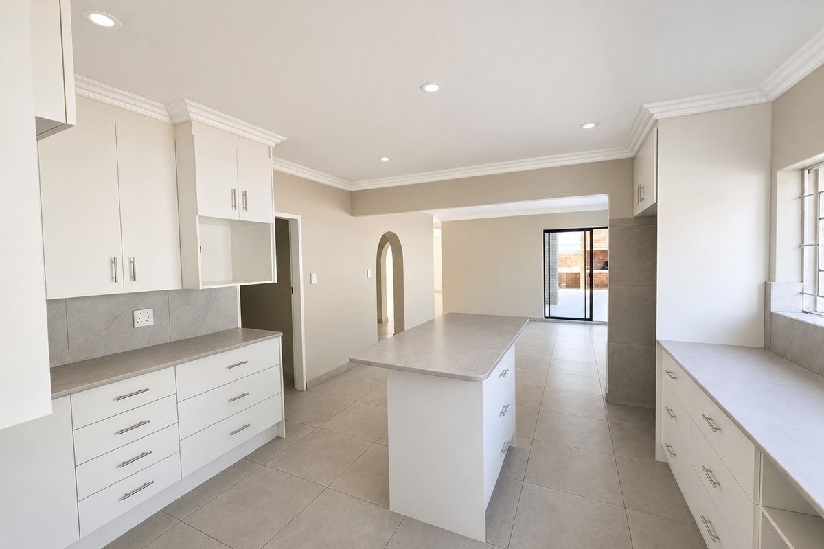 A bright, modern, and empty kitchen featuring clean white cabinetry, a central island, neutral tiled flooring, and recessed lighting, leading to an open living area.
