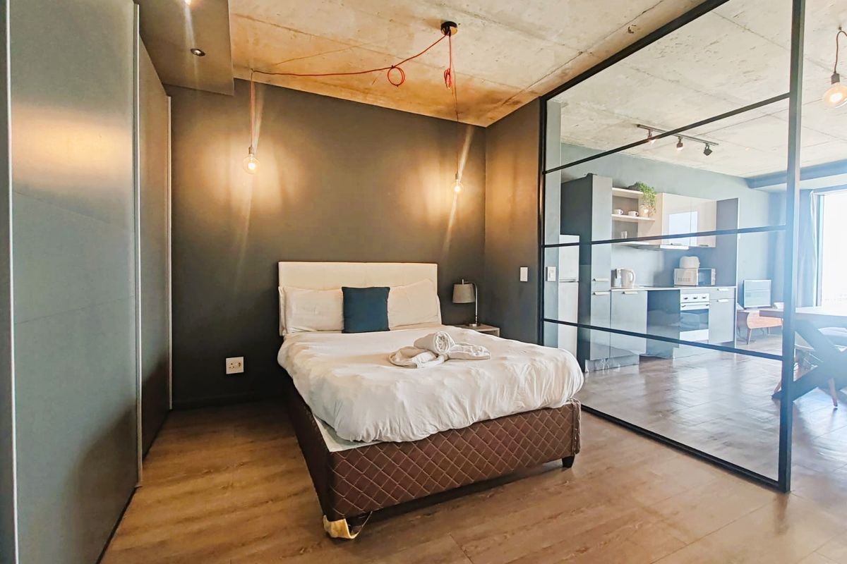 Modern bedroom featuring an exposed concrete ceiling, sleek built-in wardrobes, and a stylish glass partition wall separating the space from the adjacent living area.