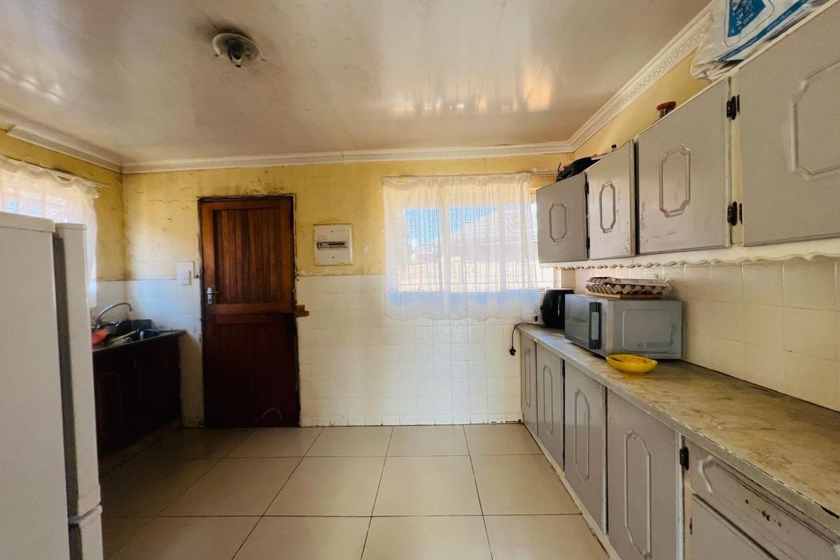 A dated kitchen featuring tiled flooring, built-in cabinetry, and a tiled splashback, requiring cosmetic updates and repairs to the wall surfaces.