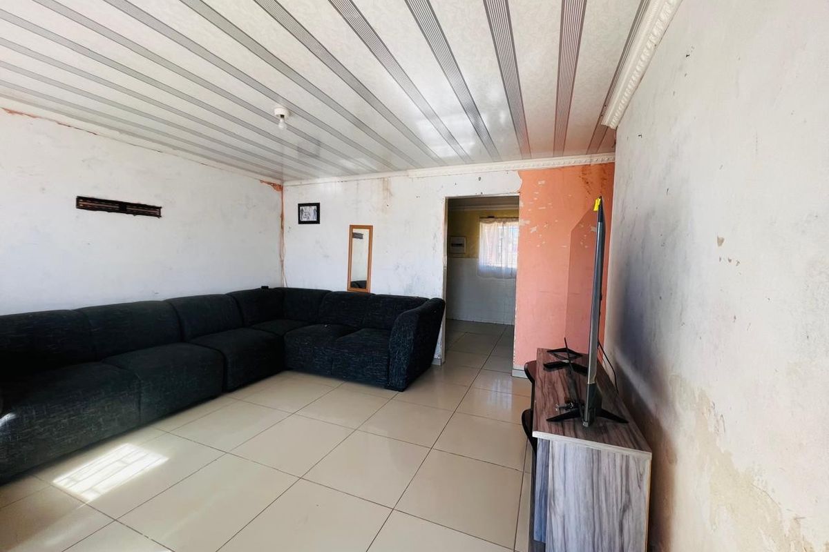 Living room featuring tiled flooring and PVC ceiling panels, currently requiring significant wall repairs and cosmetic updates to improve the overall condition.