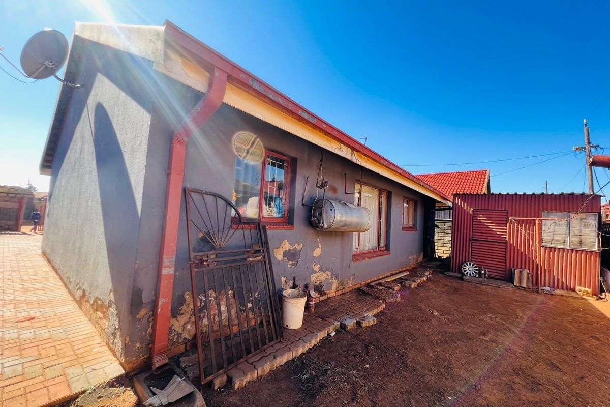 Rear exterior view of the property showing masonry walls with peeling paint, external geyser, and a corrugated metal storage structure.
