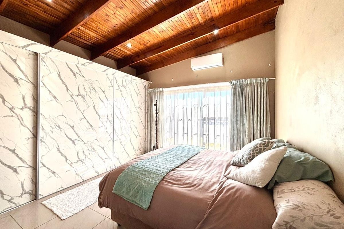 A well-maintained bedroom featuring a striking exposed timber beam ceiling, large built-in marble-finish sliding wardrobe, and wall-mounted air conditioning.
