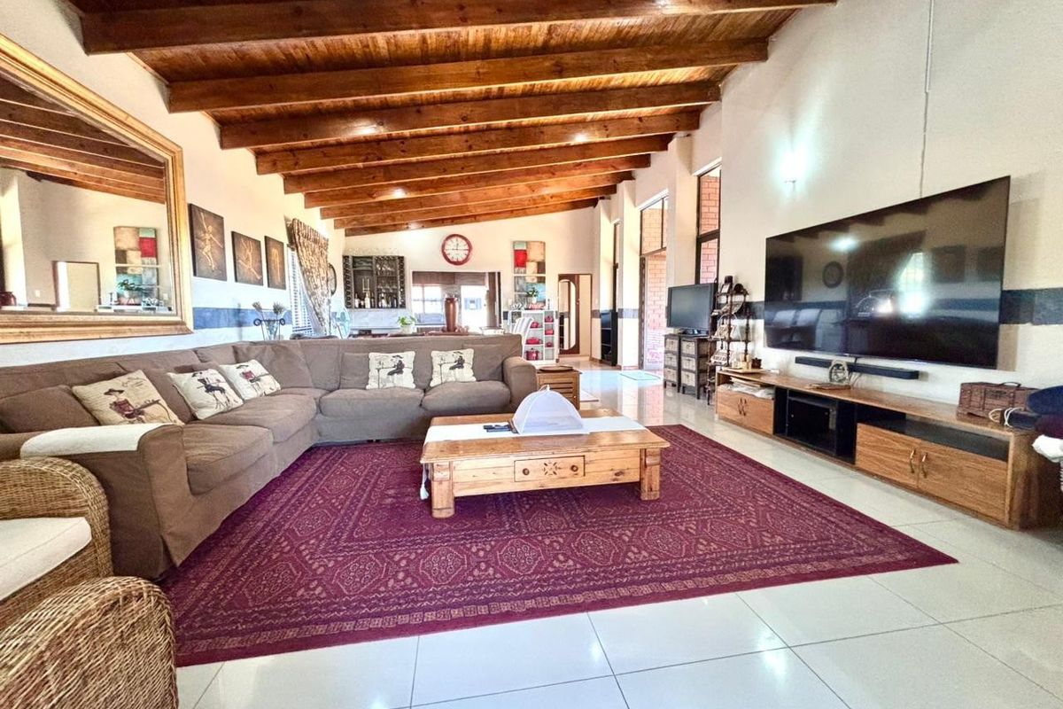 Spacious living room featuring high exposed timber beam ceilings, large format floor tiles, and a built-in media console.