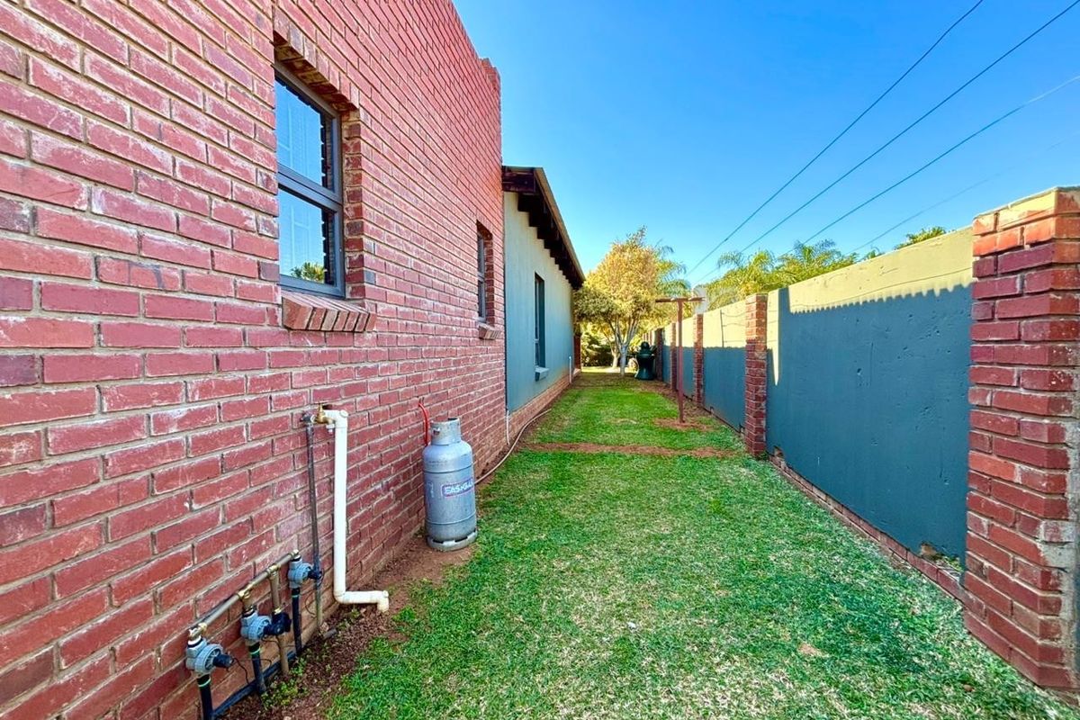 A side garden pathway featuring a red brick exterior wall, boundary wall, and external utility connections.