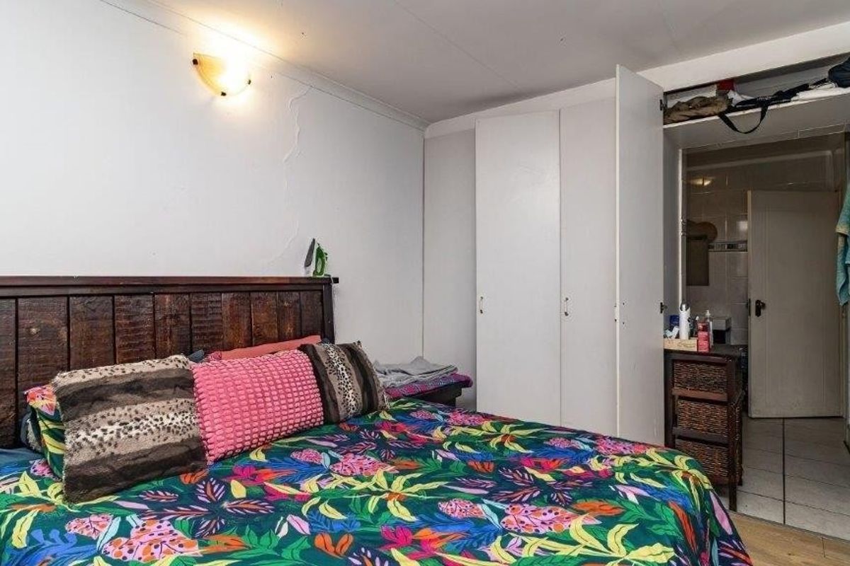 Bedroom featuring built-in cupboards and access to an en-suite bathroom, showing signs of wear including visible wall cracks.