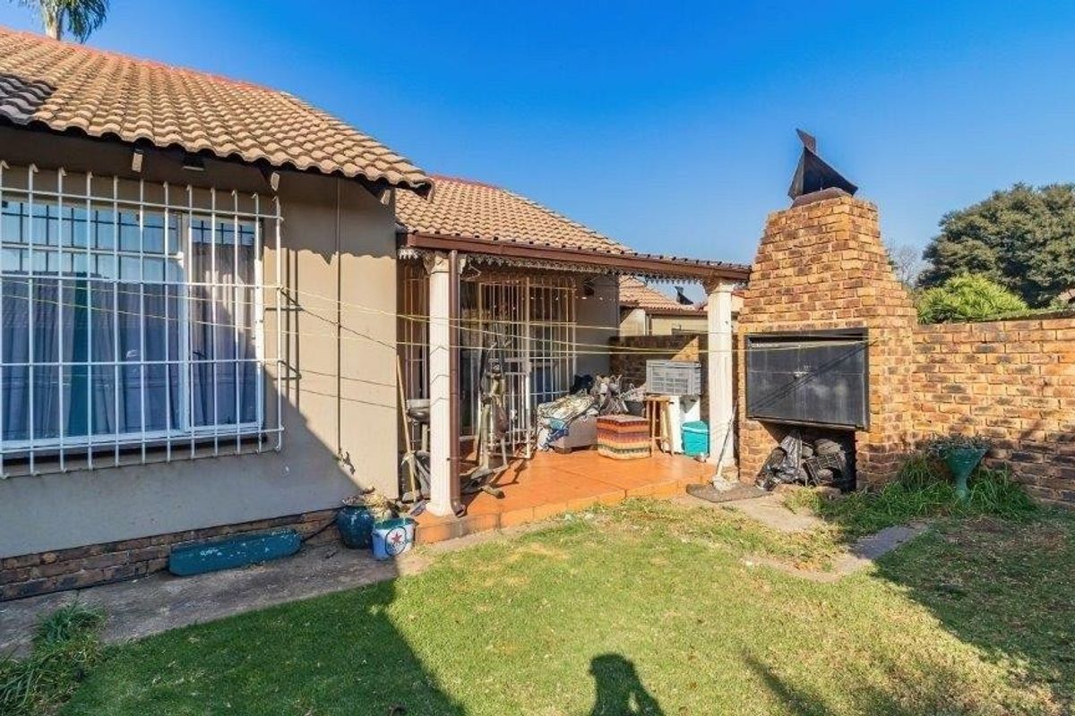 Rear exterior view of the townhouse featuring a covered patio, a brick built-in braai, and a private garden area with boundary walling.