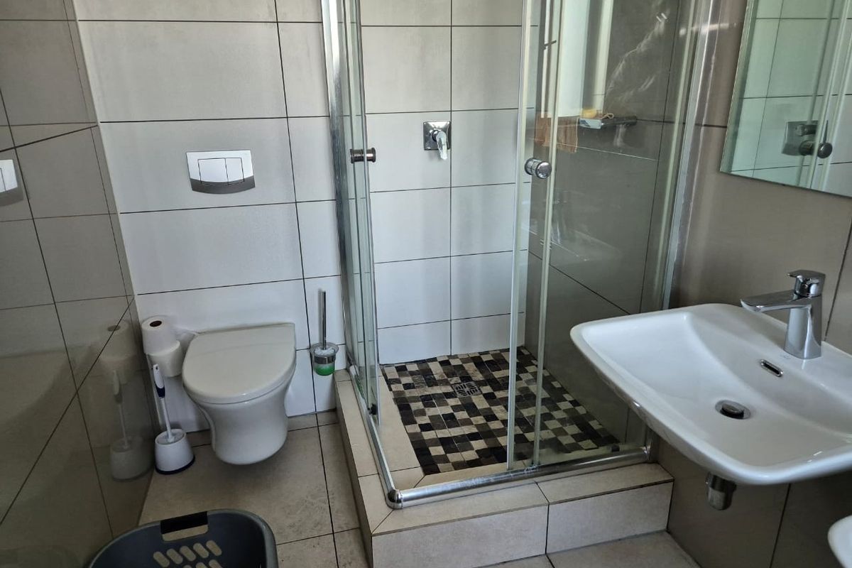 A modern bathroom featuring a wall-mounted toilet, a glass-enclosed shower with decorative floor tiling, and a wall-mounted basin with chrome fixtures.