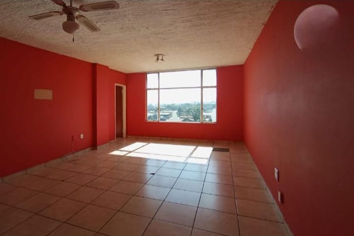 An empty, spacious living area featuring tiled flooring, a ceiling fan, and a large window providing natural light.