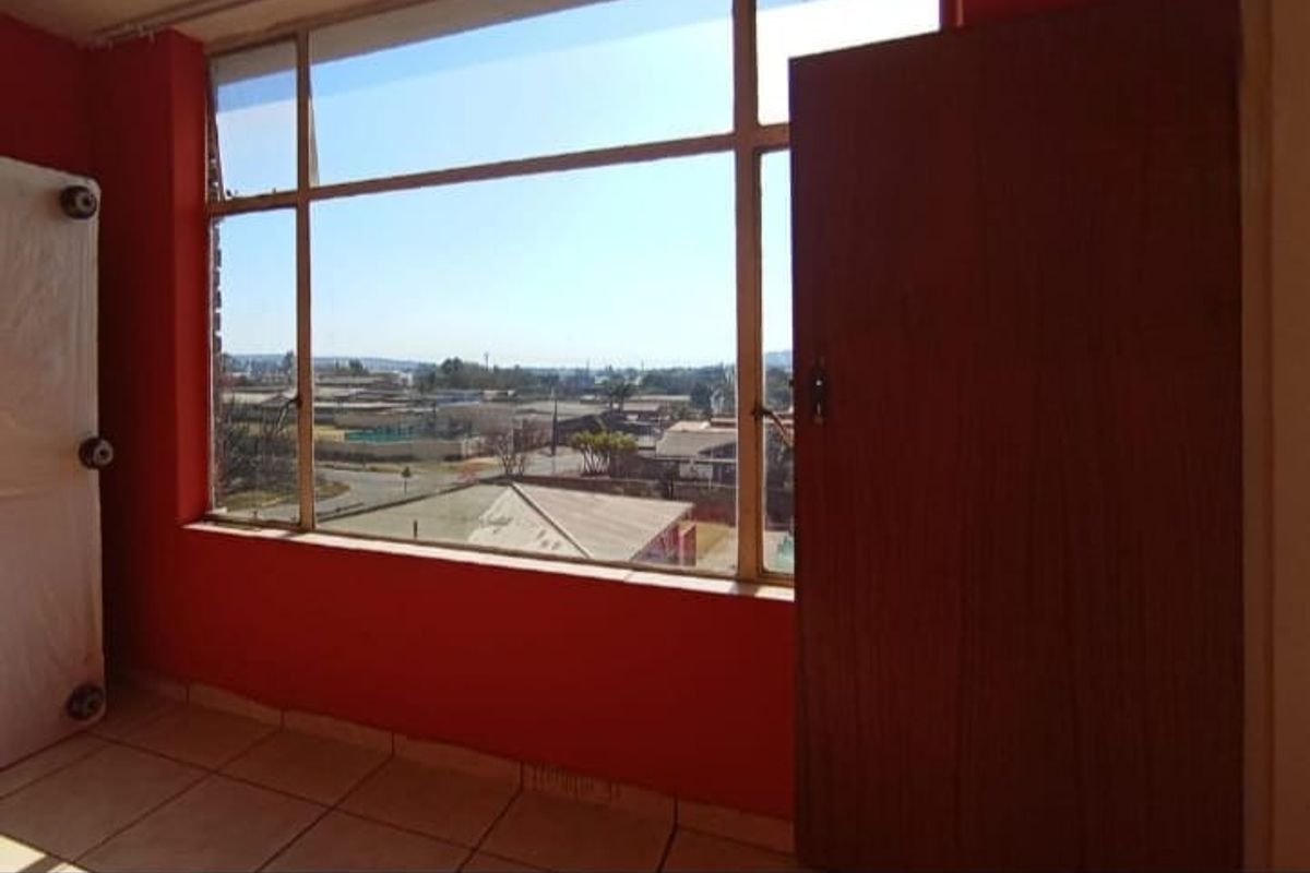 An empty bedroom featuring large windows with an exterior view, tiled flooring, and a bold red wall finish.