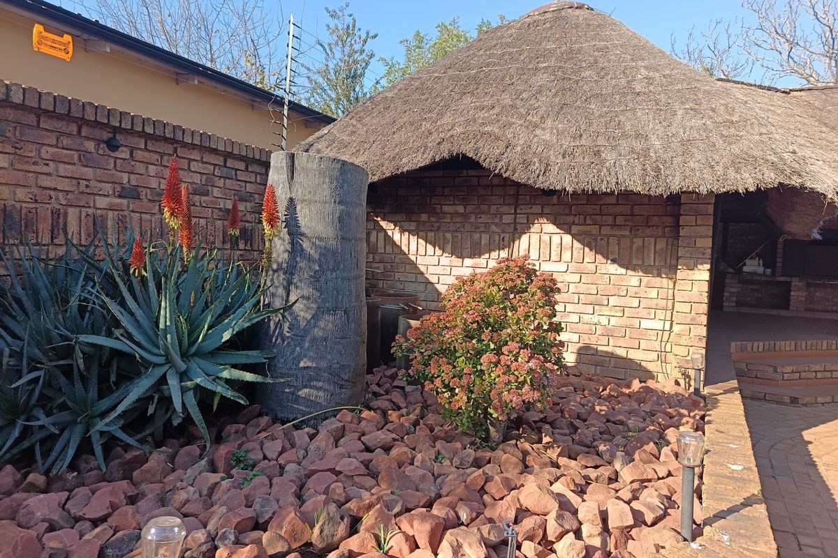 Rear garden area featuring a thatched lapa structure, brick boundary wall with electric fencing, and a paved patio with a built-in braai.
