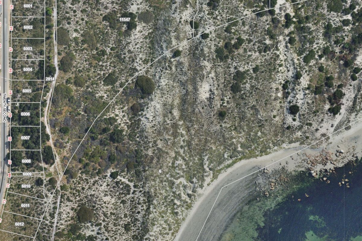 Aerial view of a vacant residential land parcel situated in a coastal location, showing property boundaries and surrounding terrain.