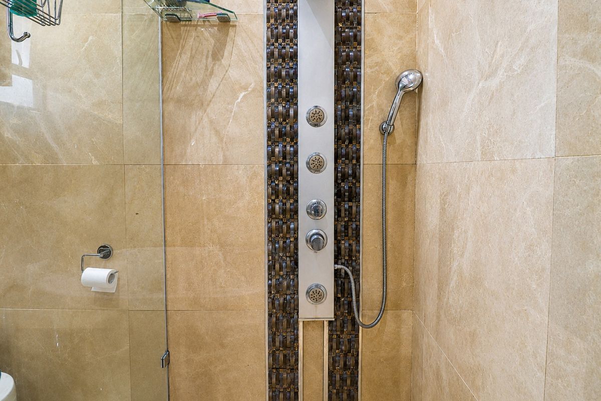 A modern bathroom shower enclosure featuring a vertical multi-jet shower panel, handheld shower head, and neutral-toned wall tiles.