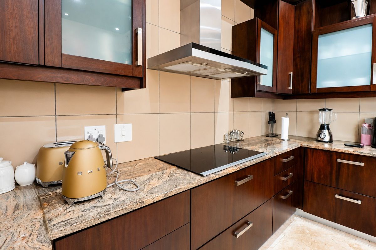 A well-maintained kitchen featuring dark wood cabinetry, granite countertops, a ceramic tile backsplash, and a modern stainless steel extractor fan over an induction hob.