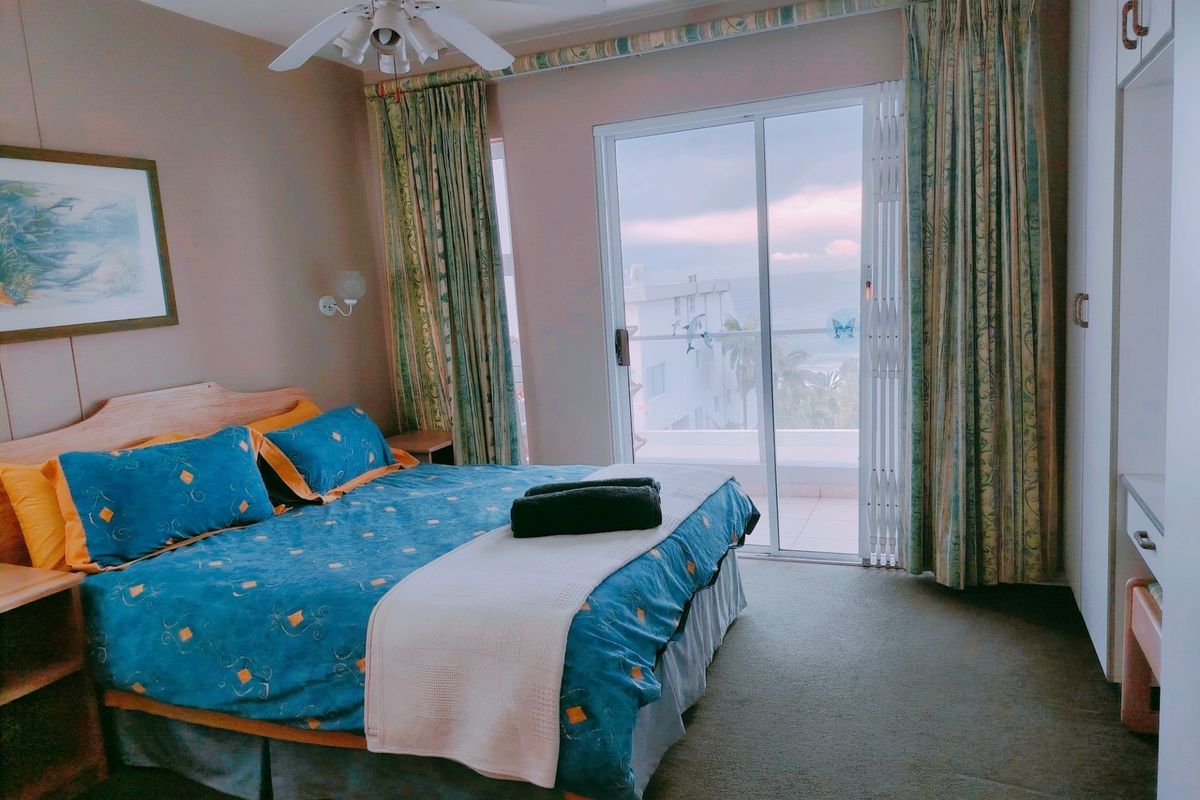 A bedroom featuring a ceiling fan, built-in wardrobe, and sliding glass doors that open onto a balcony with ocean views.