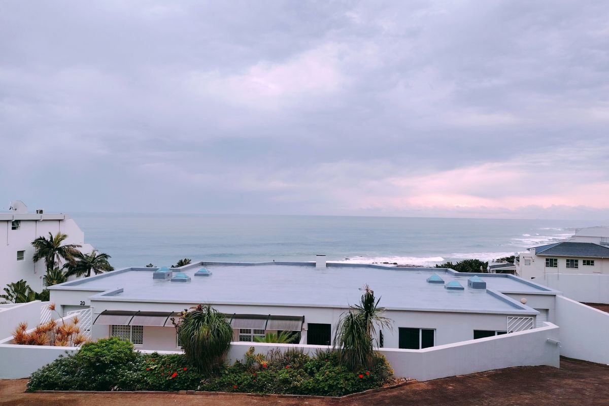 An elevated view of the apartment complex featuring a flat roof with skylights, overlooking the ocean coastline.