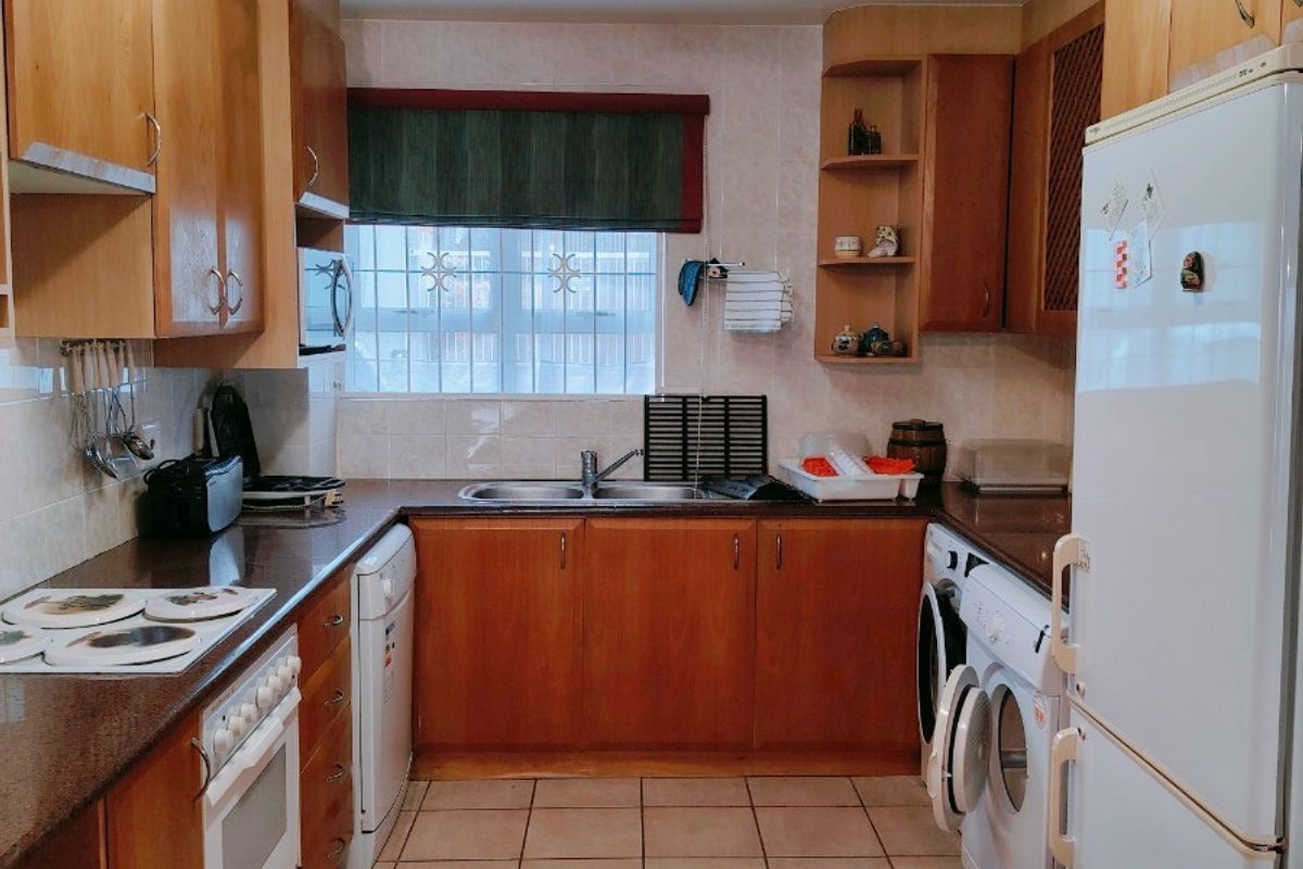 A functional kitchen featuring wooden cabinetry, tiled flooring, a double bowl sink, and integrated appliances including an oven and hob.