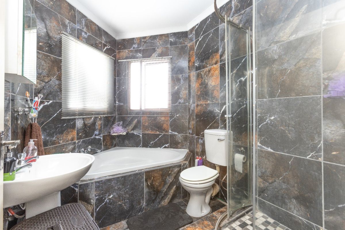 A compact bathroom featuring dark marble-effect wall tiles, a corner bathtub, a separate glass shower enclosure, and a pedestal basin.