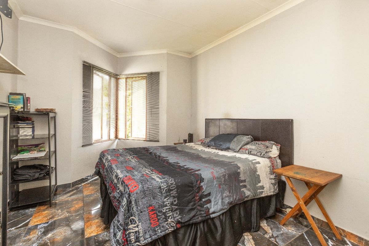 A bedroom featuring tiled flooring, coving, and venetian blinds on the corner windows, providing a functional space with neutral wall finishes.