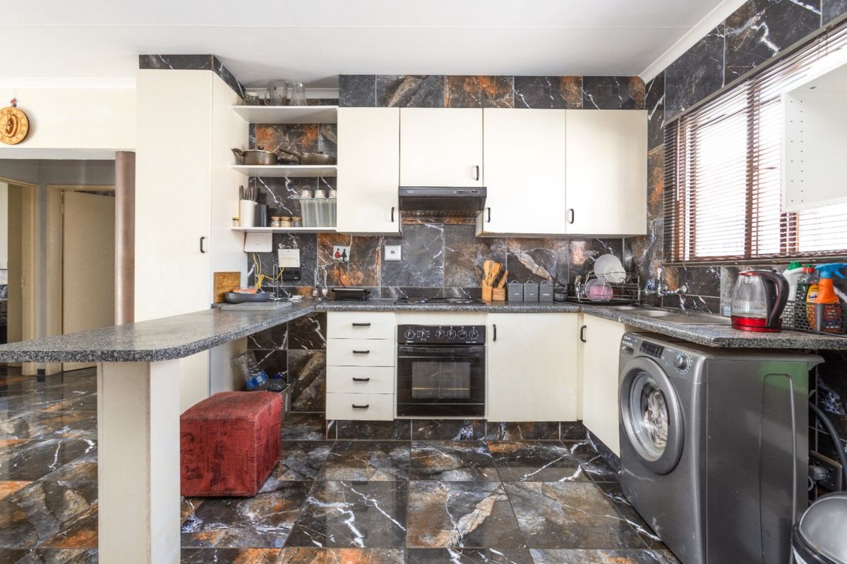 A functional kitchen featuring built-in cabinetry, an integrated oven and hob, and distinctive marble-effect tiling throughout the floor and splashback areas.