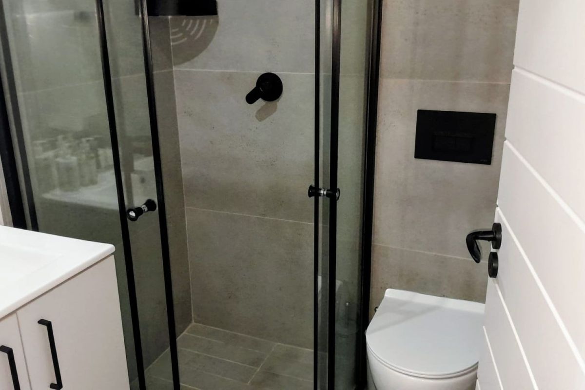 Modern bathroom featuring a glass shower enclosure, wall-mounted toilet, and a sleek vanity cabinet with contemporary black matte fixtures and neutral tiling.