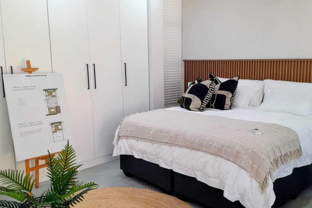 A modern bedroom featuring floor-to-ceiling built-in cupboards, a contemporary slatted timber headboard, and clean white finishes.
