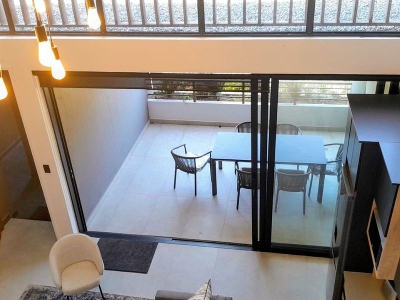 Modern open-plan living area featuring high ceilings, pendant lighting, and large sliding glass doors that open onto a private tiled balcony.