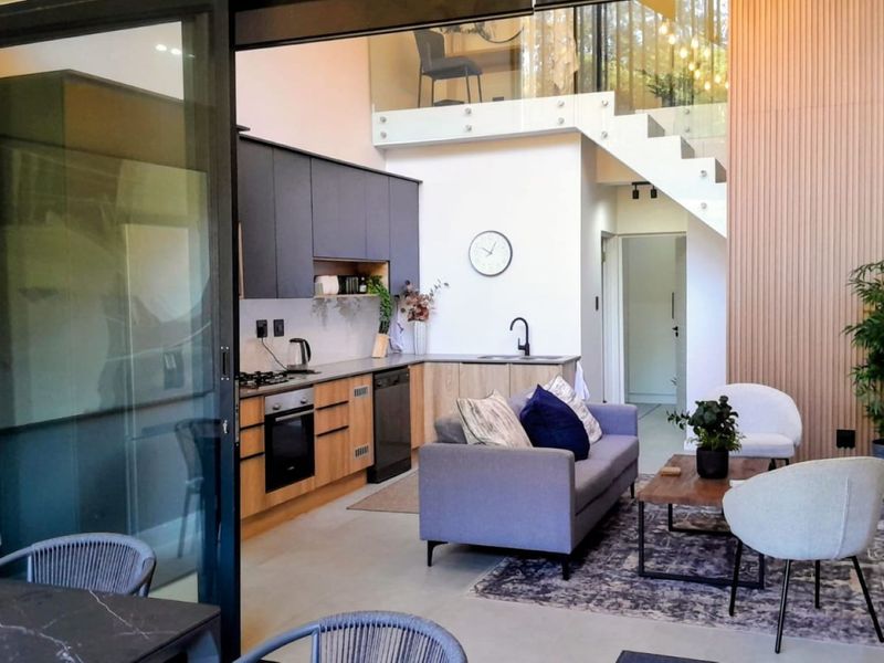 Modern open-plan living area featuring a sleek kitchen with built-in cabinetry, integrated appliances, and a striking staircase with glass balustrade and timber wall accents.