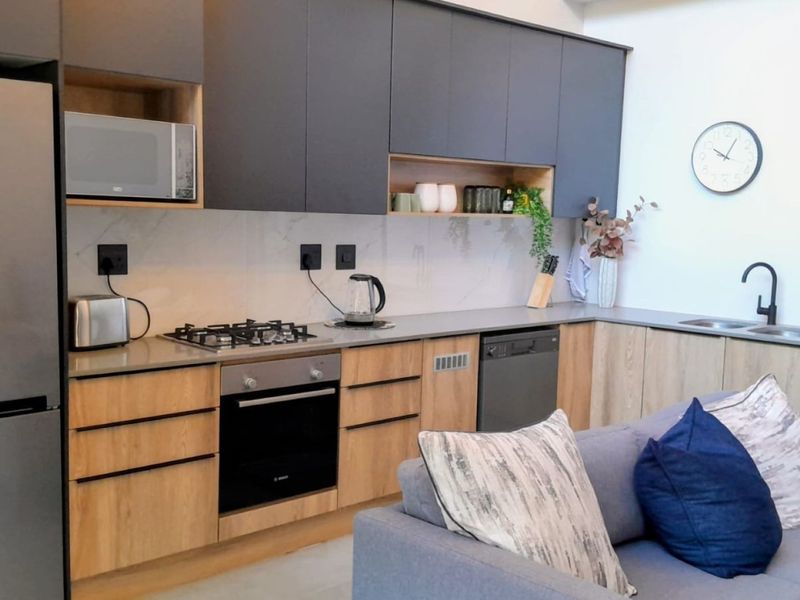 Modern open-plan kitchen featuring sleek two-tone cabinetry, stone countertops, built-in gas hob, oven, and integrated appliances, seamlessly flowing into the living area.