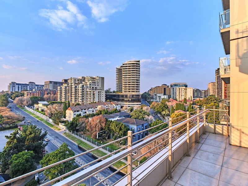 A spacious apartment balcony featuring tiled flooring and a modern metal and glass balustrade, offering expansive urban views.